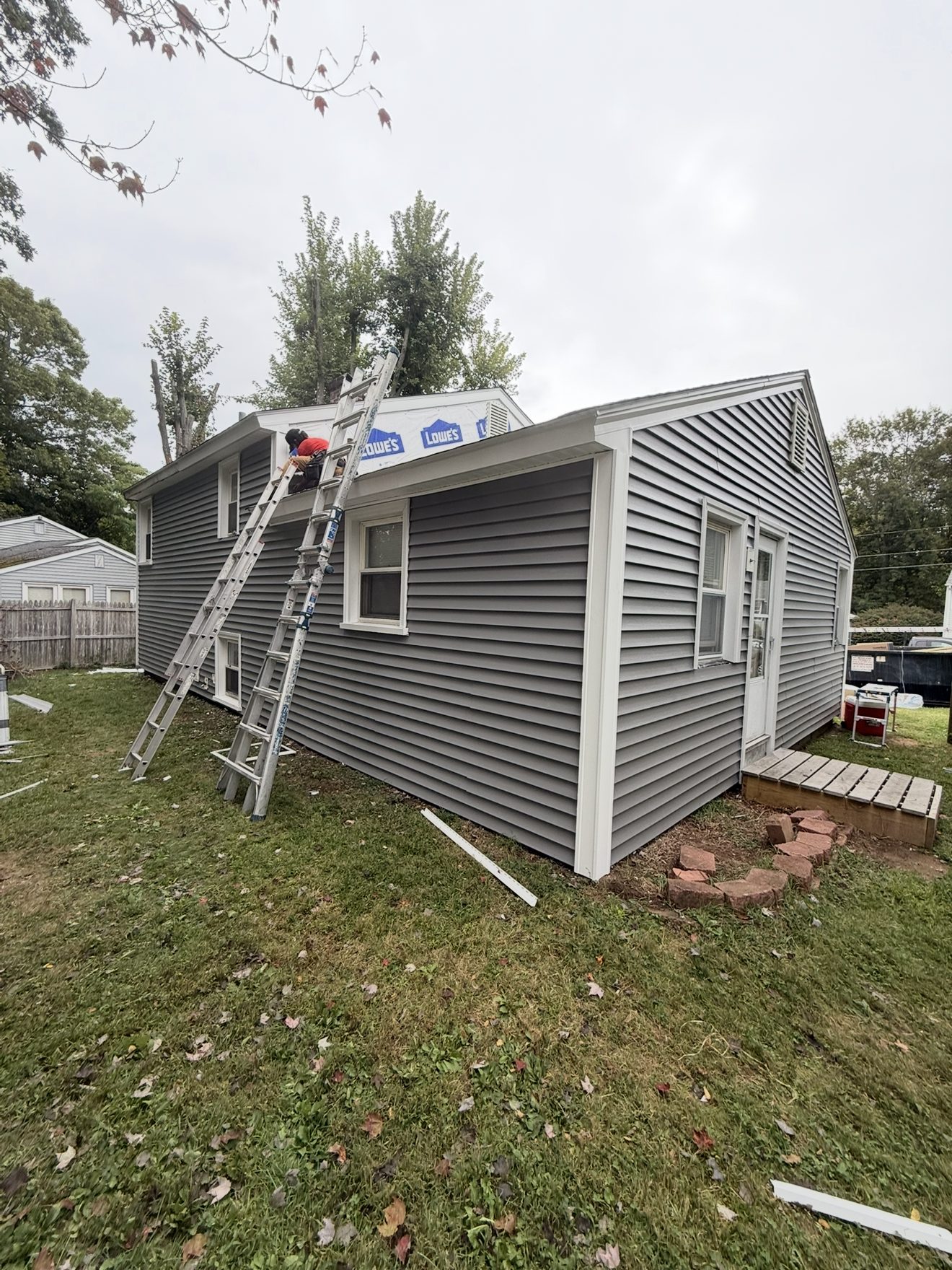 Next Gen Construction crew member working on a roof repair, ladders set against the home