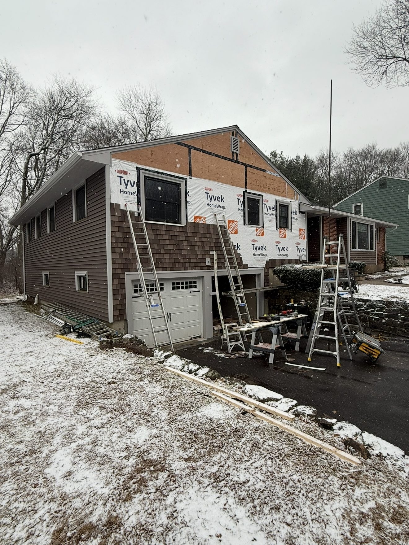 Crew installing siding over Tyvek house wrap during a winter job with snow on the ground